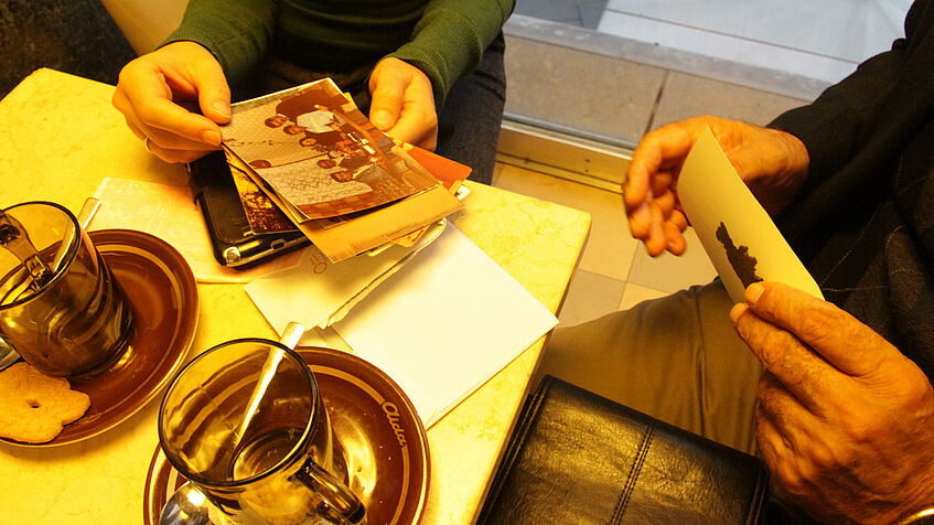 Tisch in Aida mit Kaffeetassen und Hände, die Fotos halten