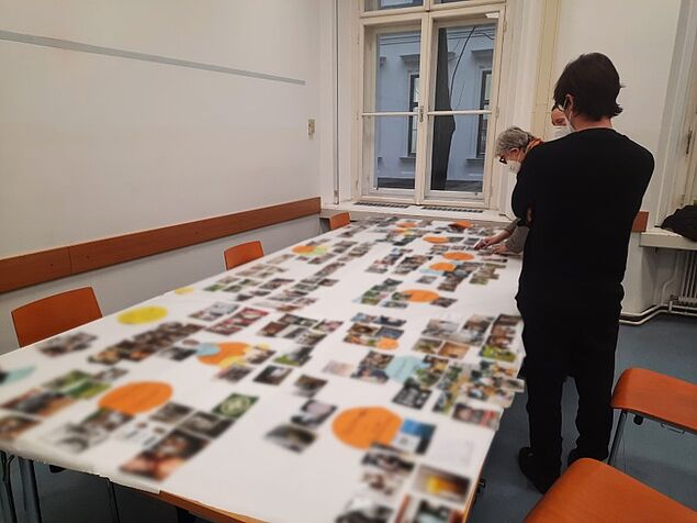 Das Projektteum beugt sich über einen großen Tisch wo die Bilder auf einem großen weißen Papier systematisch angeordnet sind.