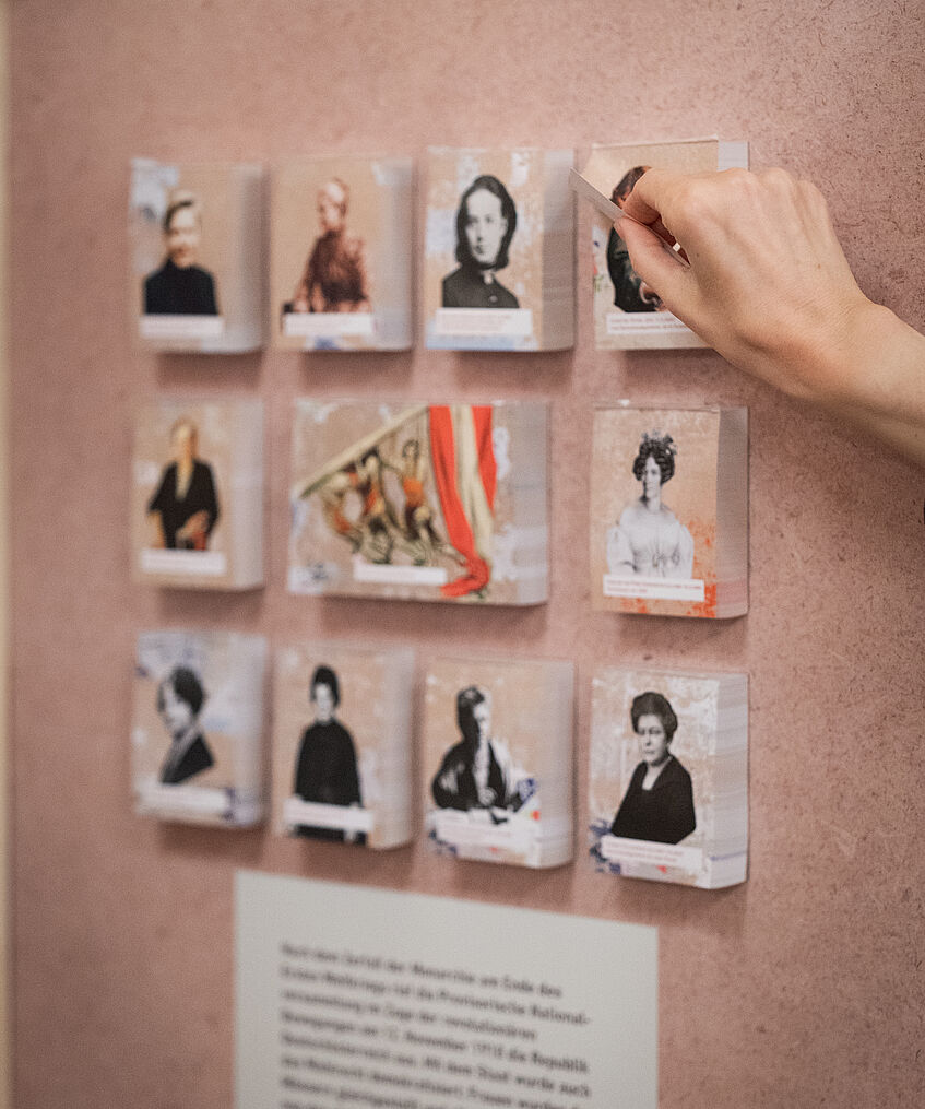 Kleine Bilder von Frauen an einer Wand, hinter den Bildern sind aufklappbare Informationen