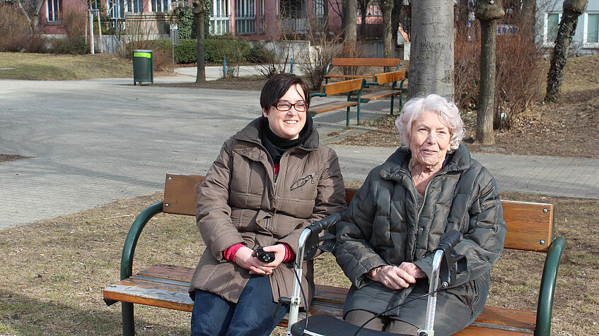 Zwei Personen sitzen bei herbstlichem Wetter auf einer Parkbank