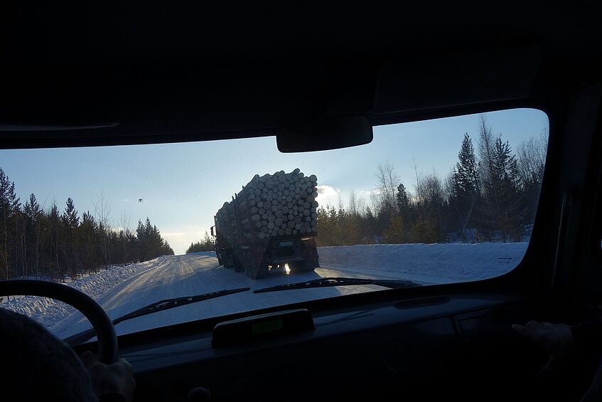 Blick aus einer Windschutzscheibe auf einen LKW, der Holzstämme in einer verschneiten Landschaft transportiert