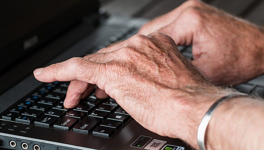 Ältere Hände tippen auf einem Laptop