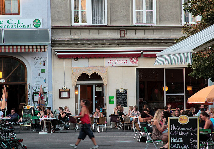 Menschen sitzen in Cafes, ein Restaurant ist im Hintergrund