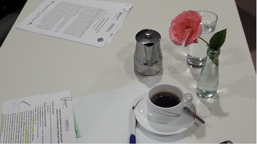 Rosa Rose, Kaffee und Infoblätter auf einem Tisch