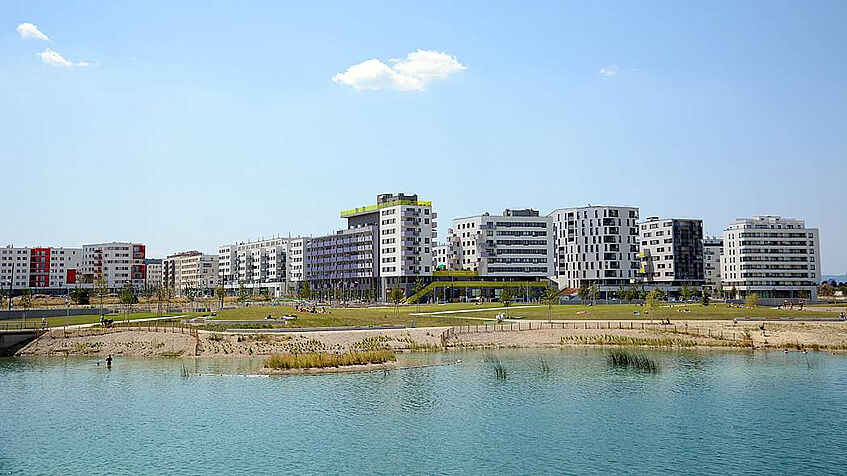 Blick über den See auf die Seestadt Aspern nach der Fertigstellung der ersten Bauphase, Sommer, blauer Himmel.