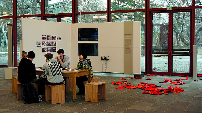 Jugendliche sitzen an einem Holztisch in einer Ausstellungshalle